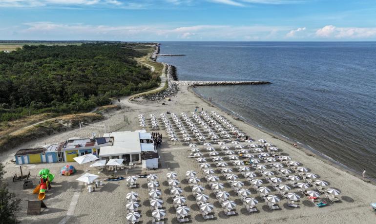 Strand mit weißen Sonnenschirmen und ruhigem Meer, Luftaufnahme.