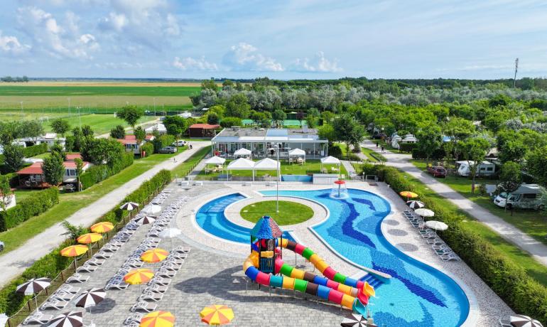 Pool mit bunten Rutschen in einem von Grün umgebenen Campingplatz.