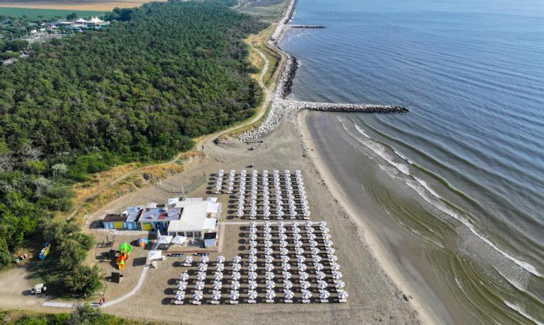 Spiaggia con ombrelloni, mare calmo e vegetazione costiera.