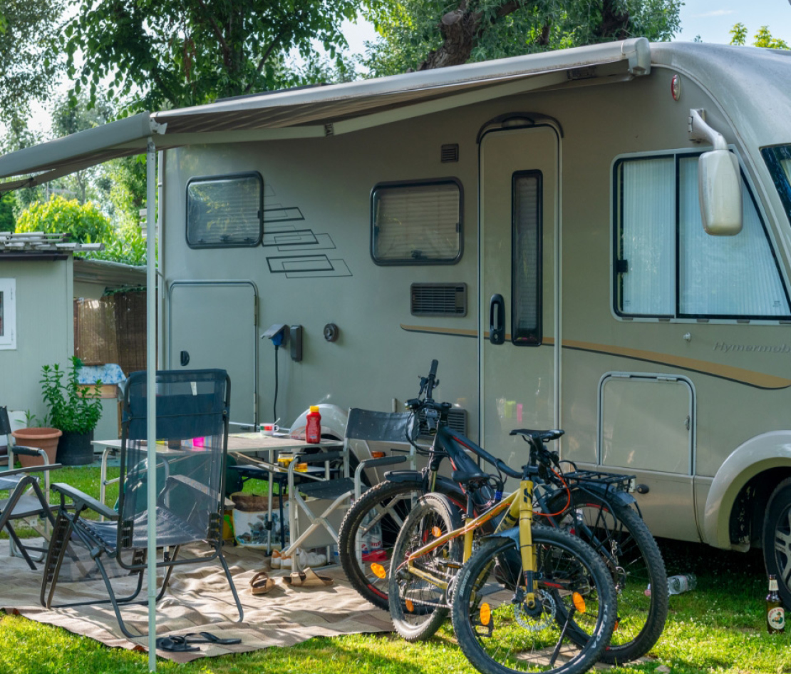 Camper con veranda, sedie e biciclette parcheggiate sul prato verde.