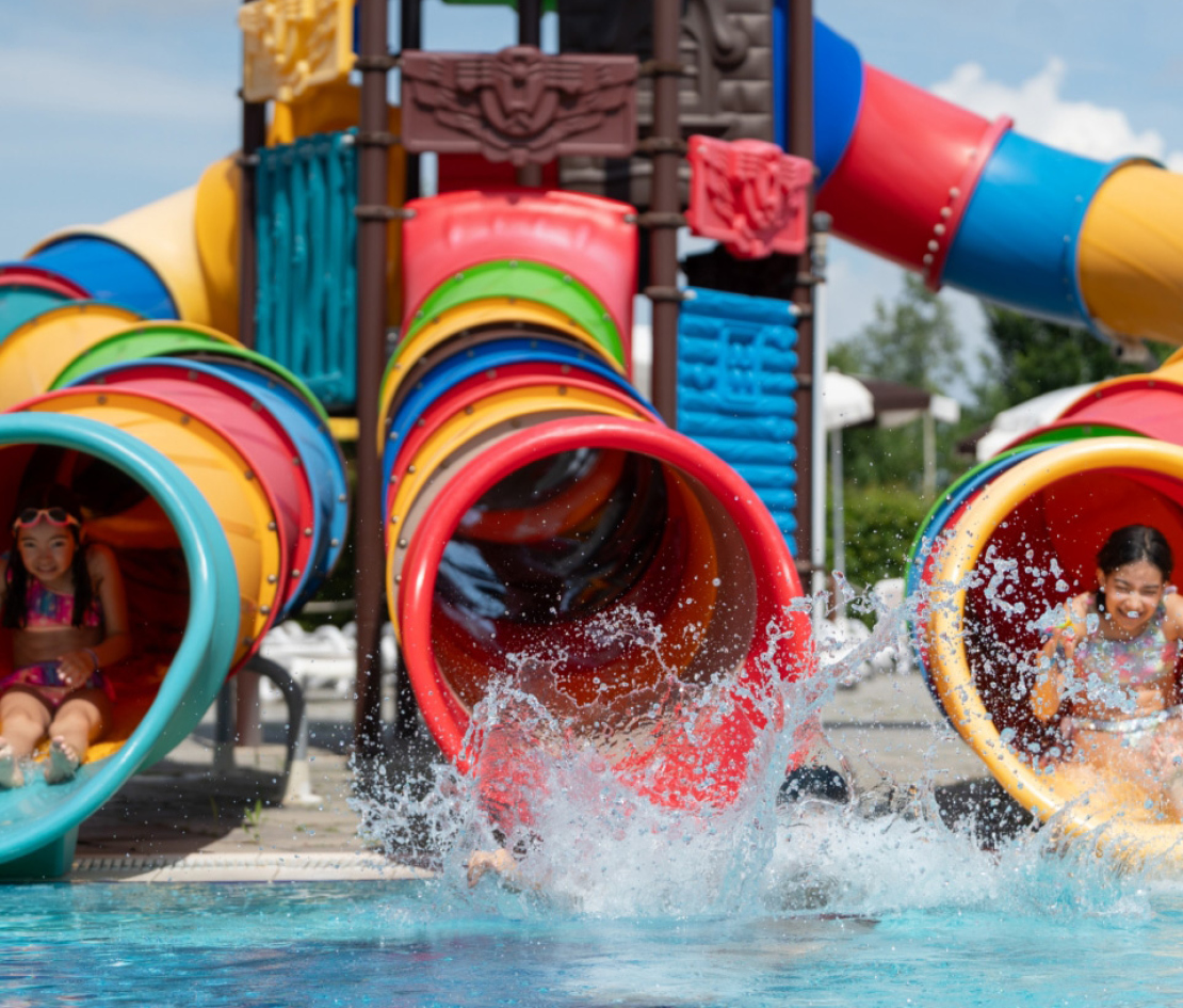 Bambini scivolano in piscina da colorati scivoli acquatici al parco giochi.