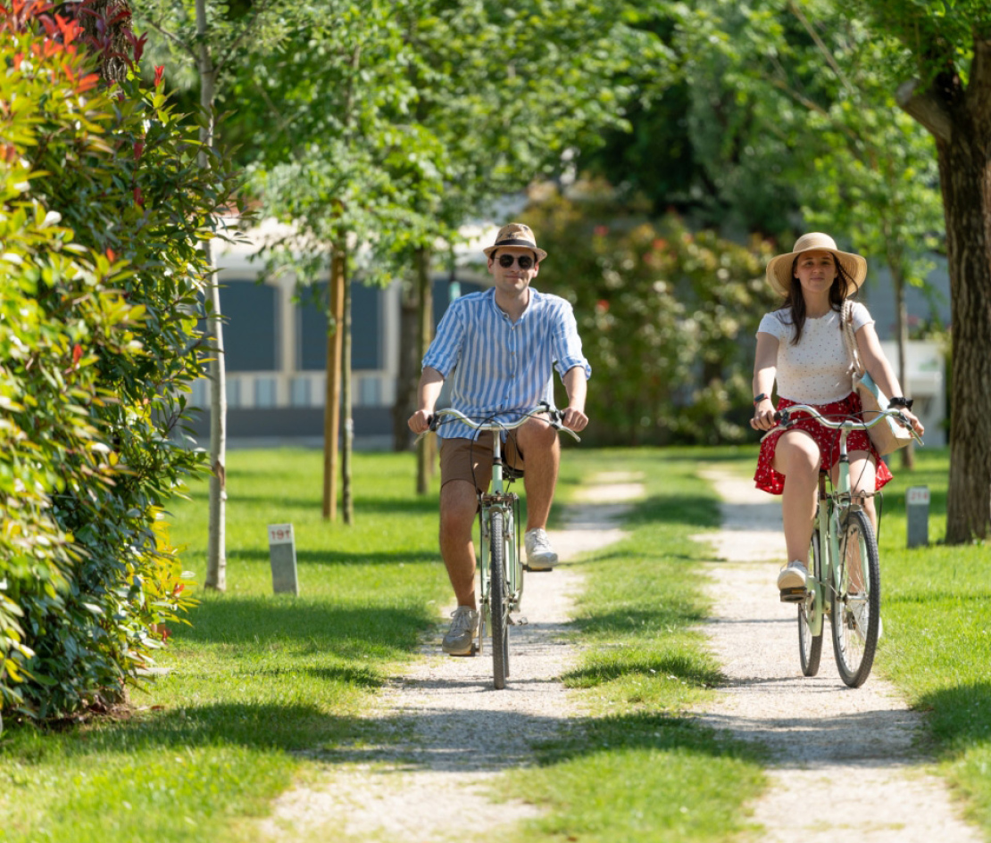 Coppia in bicicletta su un sentiero alberato in una giornata di sole.