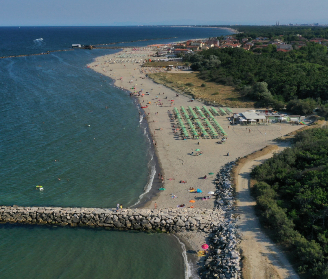 Spiaggia affollata con ombrelloni verdi, mare calmo e lungomare roccioso.