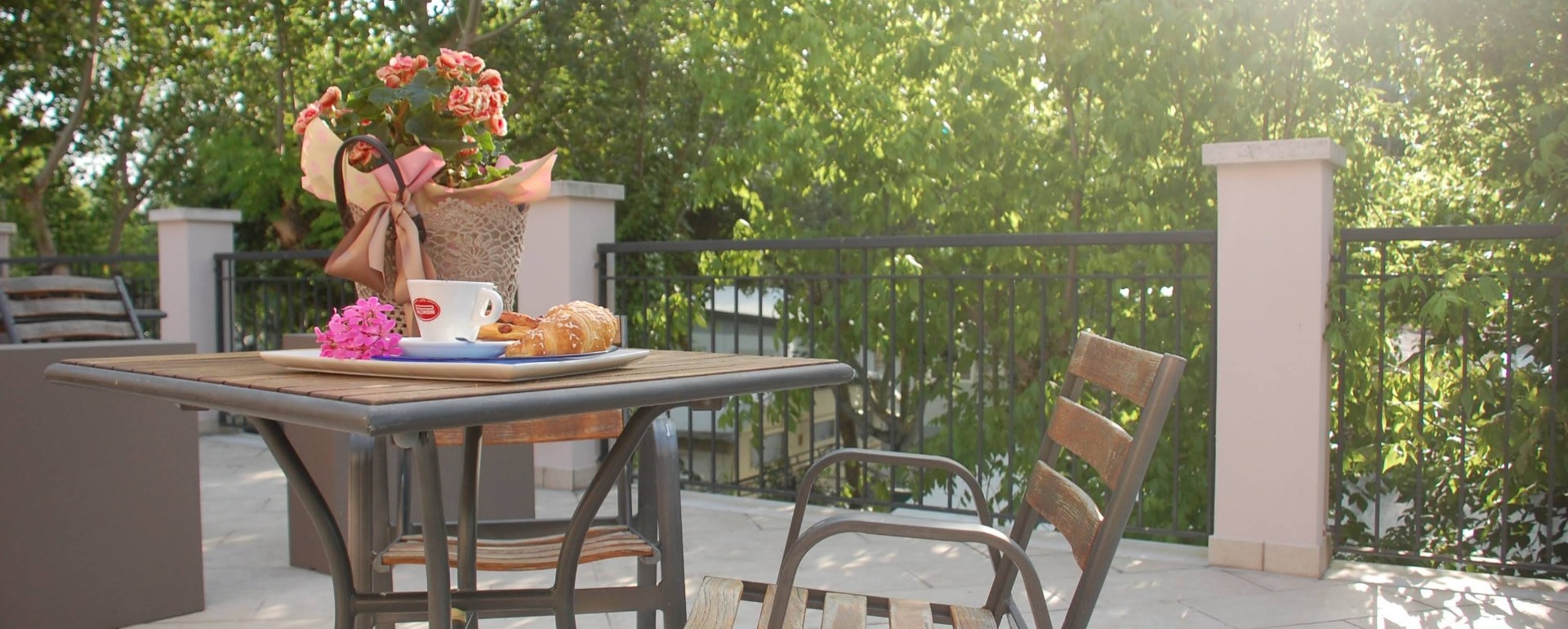 Colazione all'aperto con caffè, croissant e fiori su un tavolo.