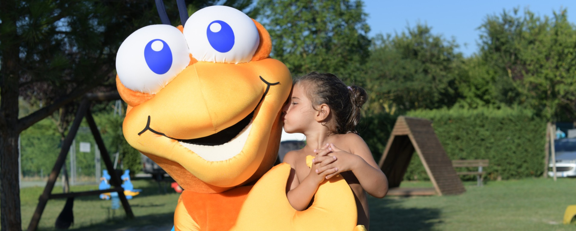 Bambina bacia un costume da mascotte arancione in un parco.