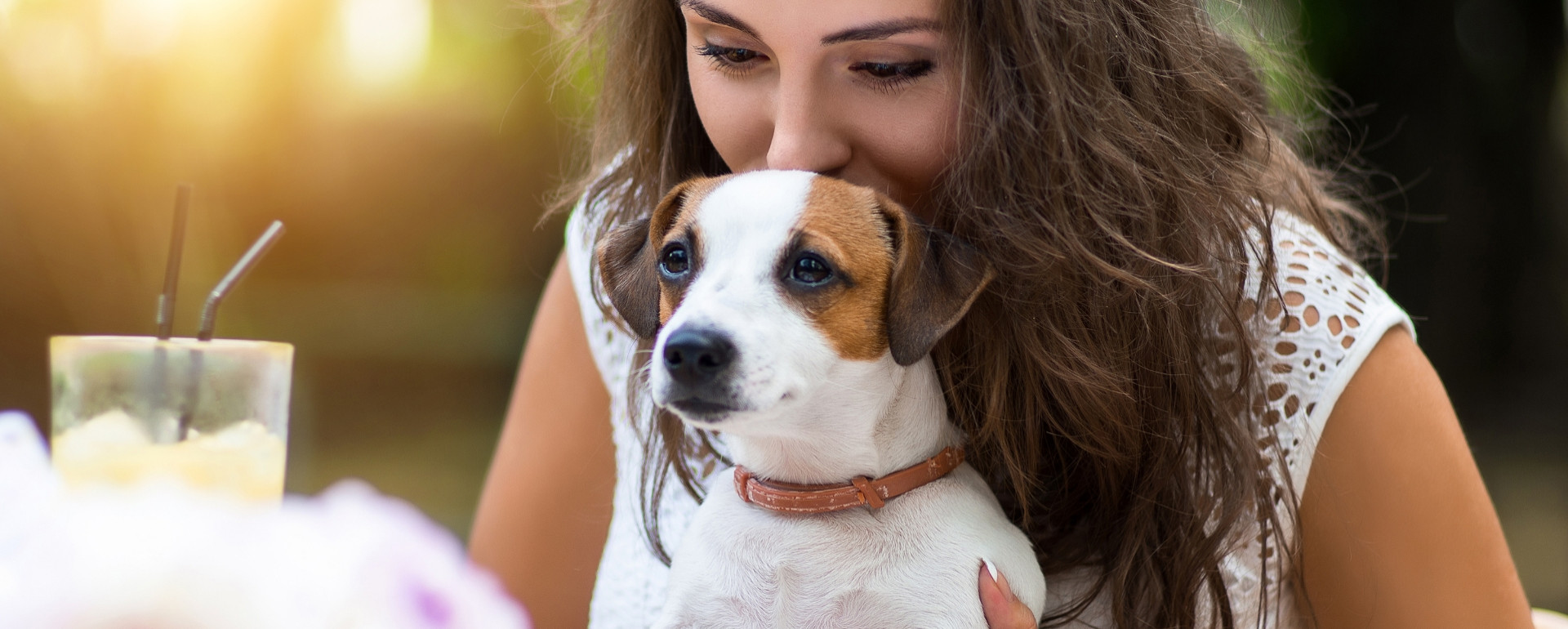 Donna abbraccia un cane, bevanda sul tavolo, atmosfera serena.