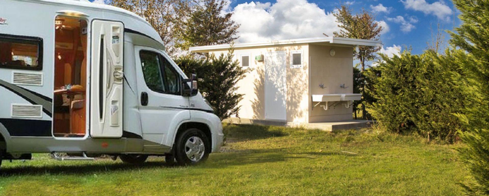 Camper vicino a un edificio con lavandini all'aperto, immerso nel verde.