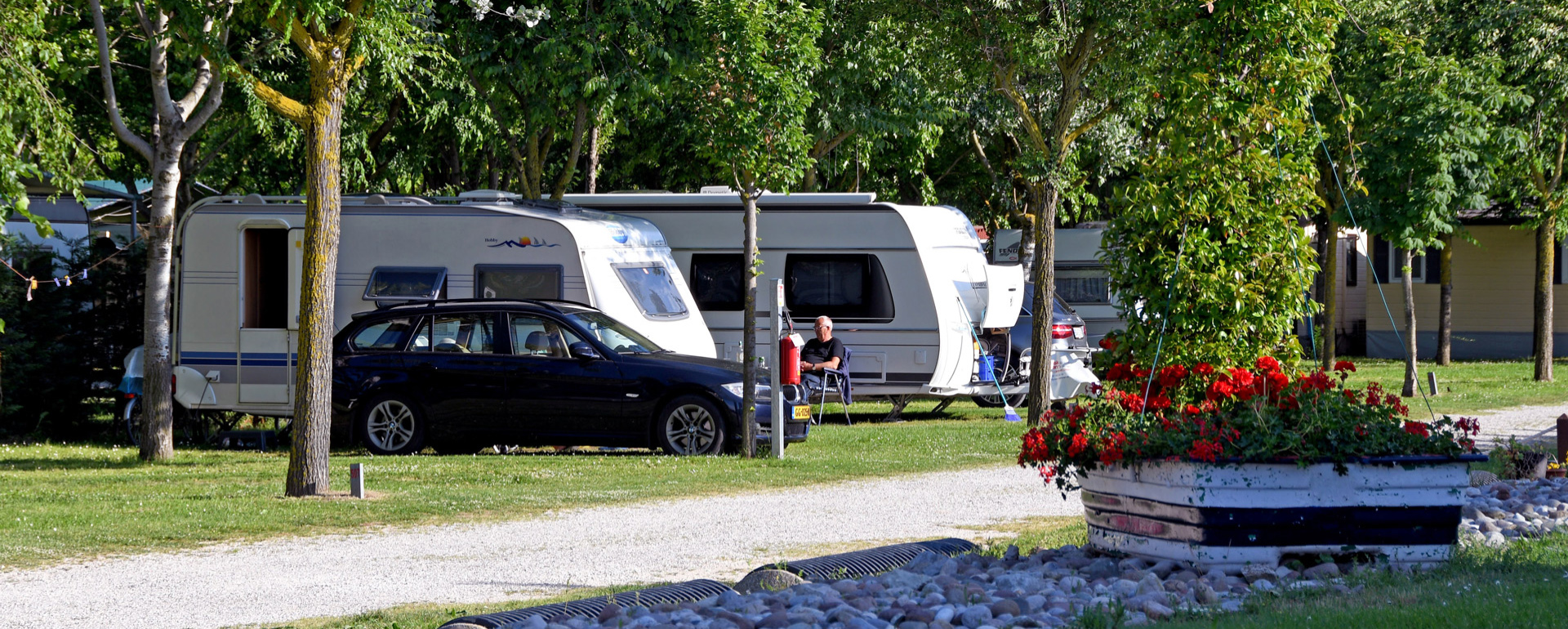 Campeggio con roulotte, auto nera e fiori rossi.