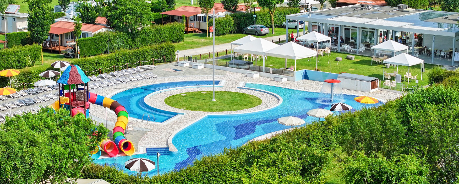 Piscina con scivoli colorati e lettini in un villaggio turistico.