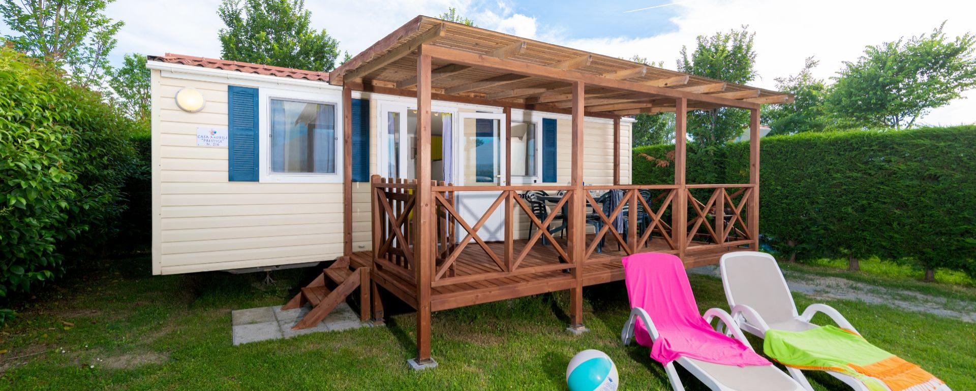 Stacaravan met veranda en ligstoelen op groen gras.