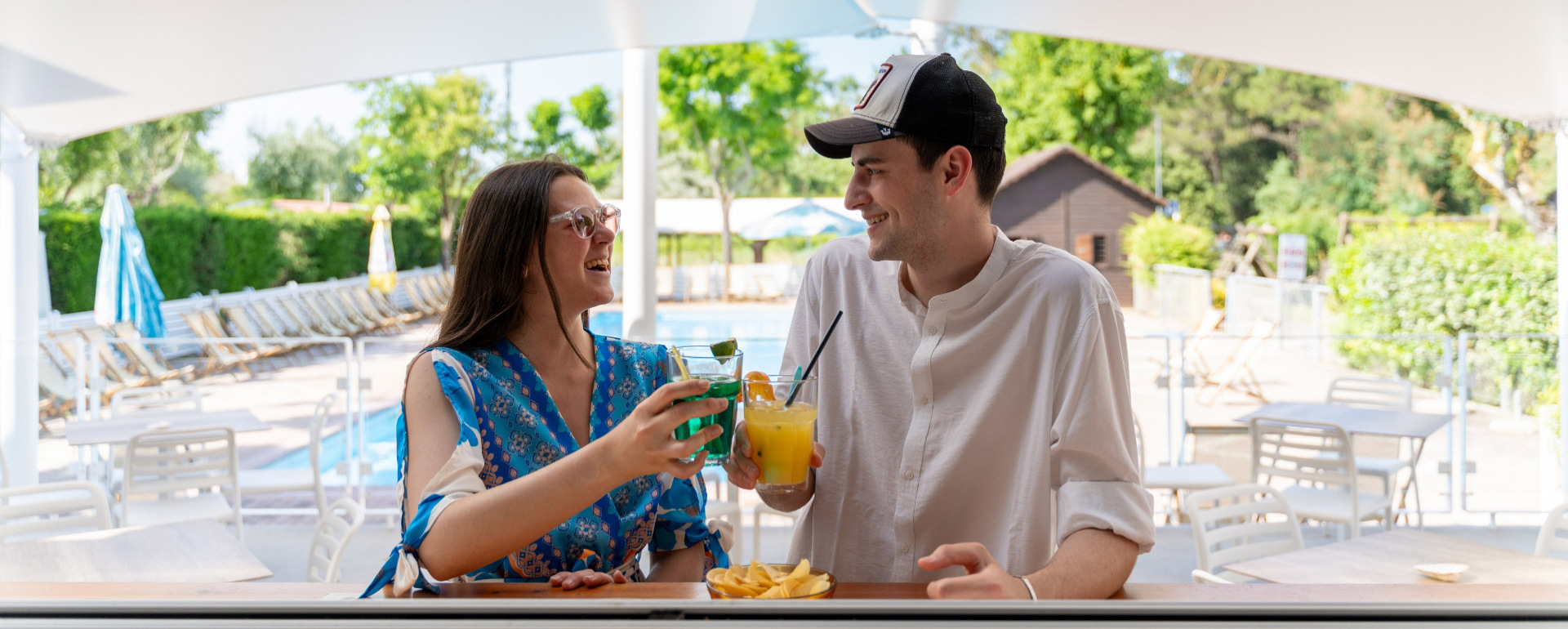 Due persone brindano con cocktail vicino a una piscina.