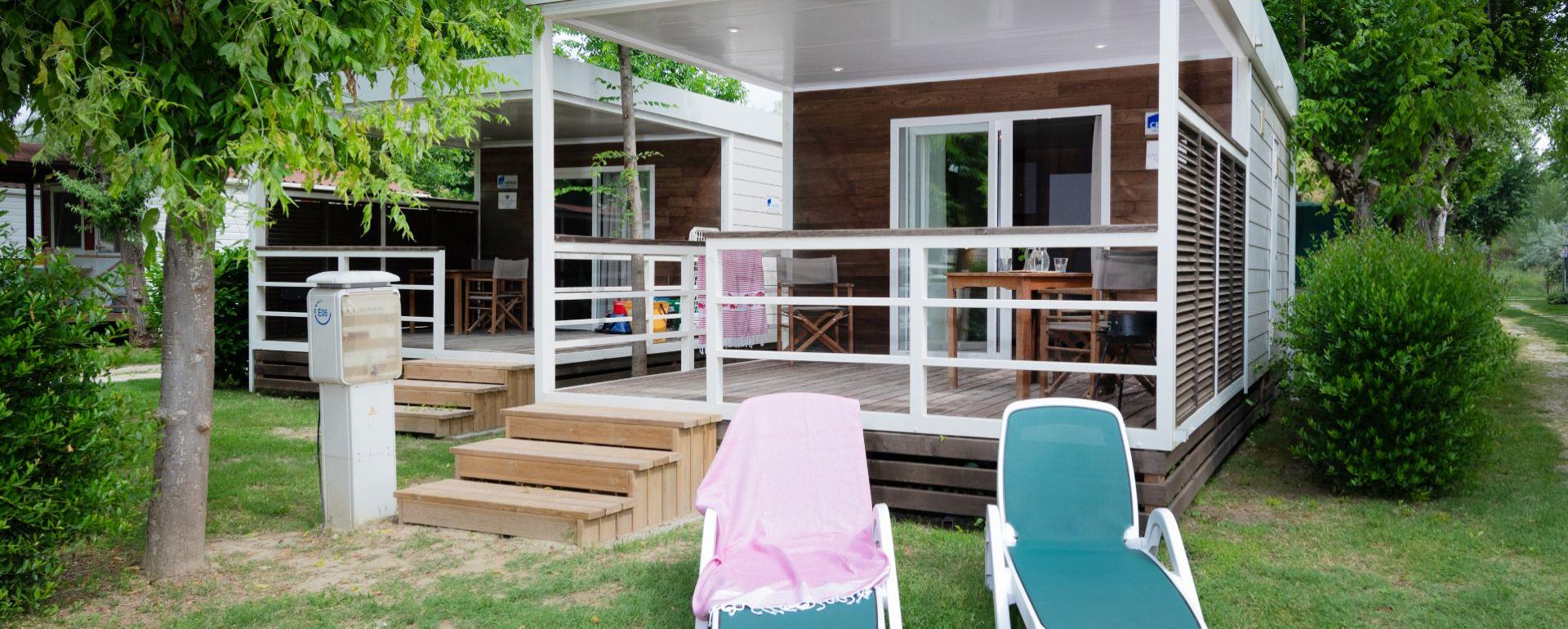 Moderne bungalow met veranda en ligstoelen in groene tuin.