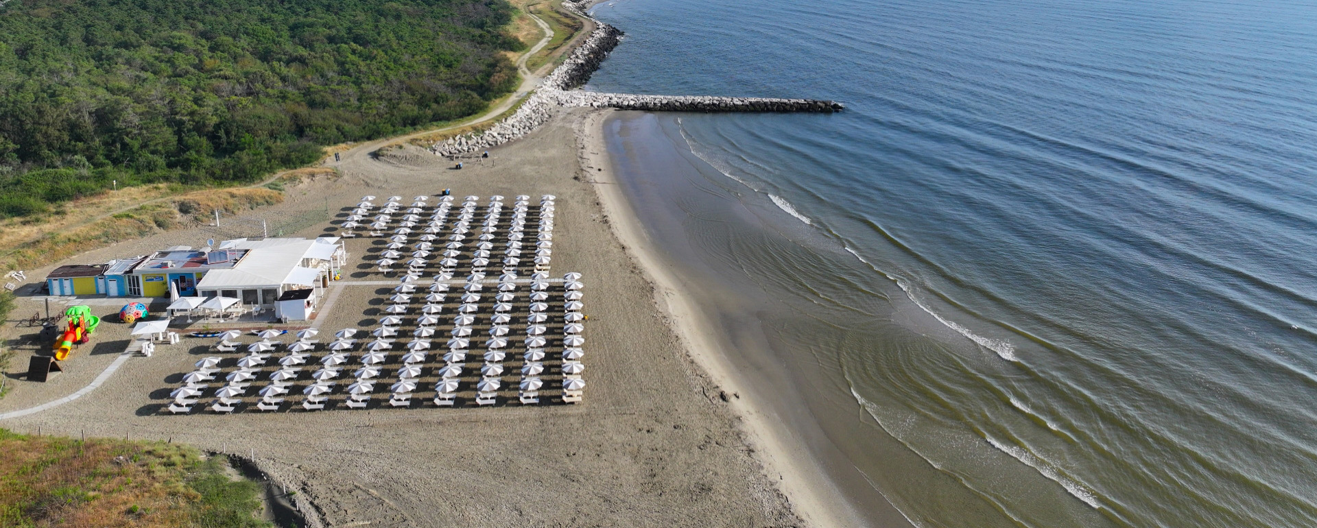 Spiaggia con ombrelloni, mare e vegetazione.