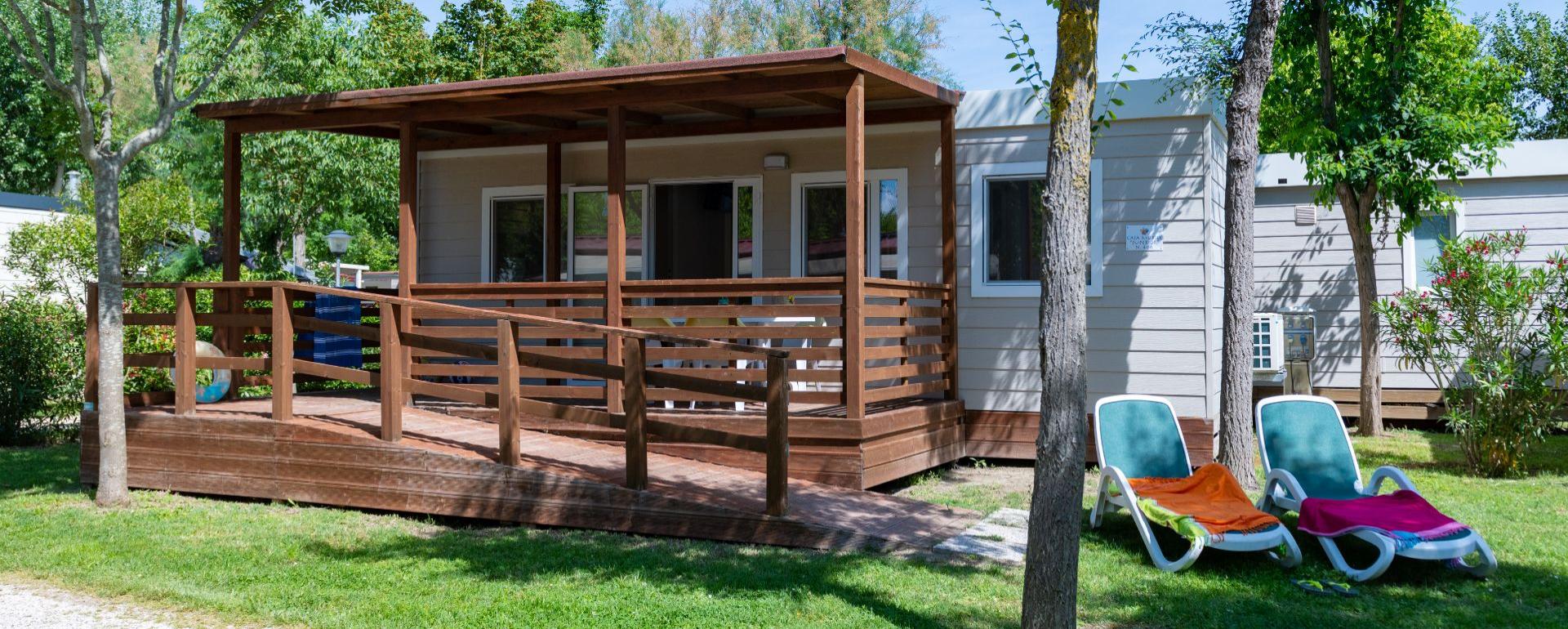 Houten hut met veranda en ligstoelen op groen gras.