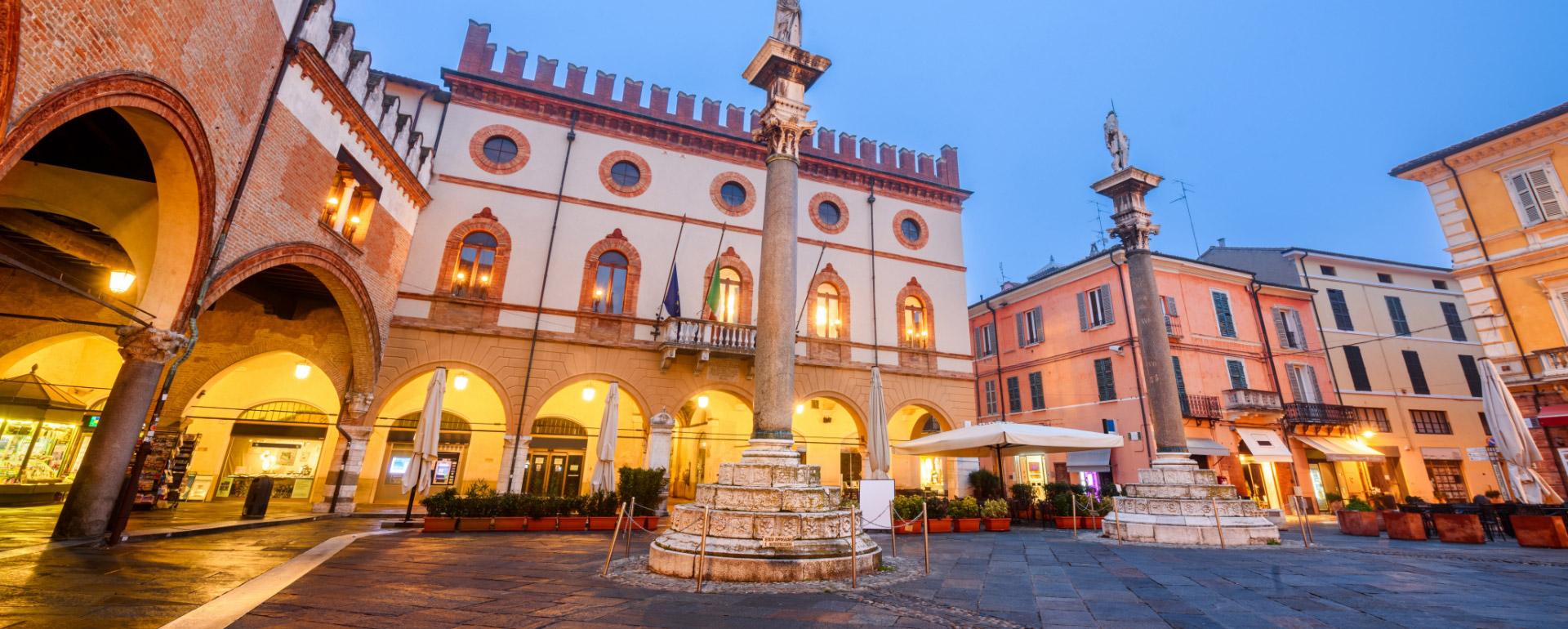 Piazza storica con colonne e architettura antica al tramonto.