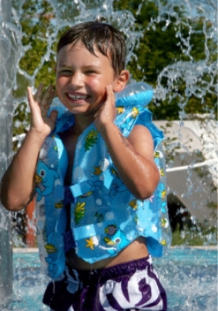 Bambino felice con giubbotto di salvataggio gioca sotto una fontana d'acqua.