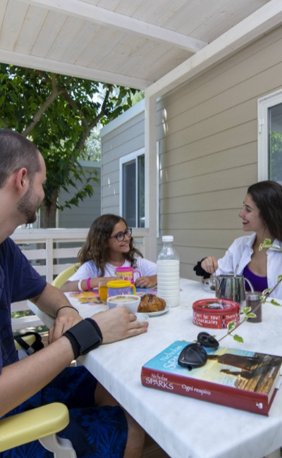 Famiglia fa colazione all'aperto, tavolo con cibo e libro di Nicholas Sparks.