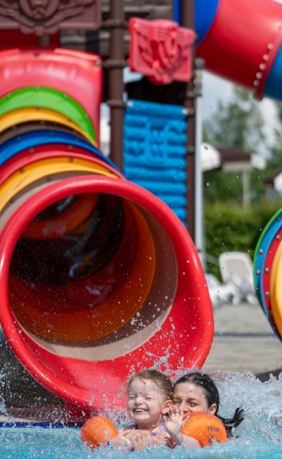 Bambini felici escono da uno scivolo colorato in un parco acquatico.