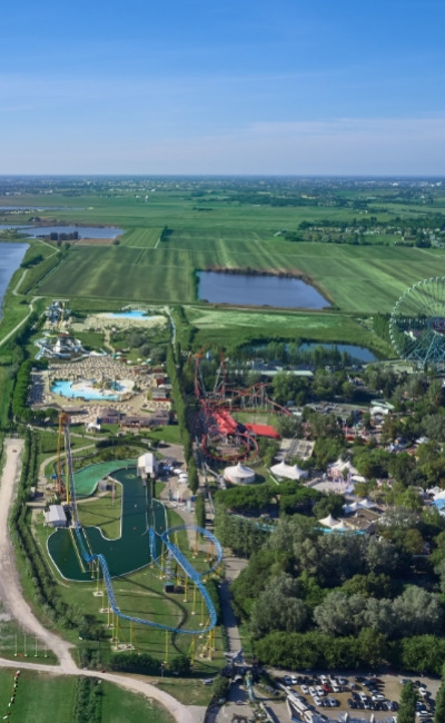 Parco divertimenti con montagne russe e laghi, immerso nel verde paesaggio rurale.