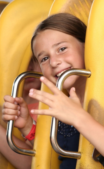 Bambina sorridente su una giostra, tenendo le maniglie di sicurezza gialle.