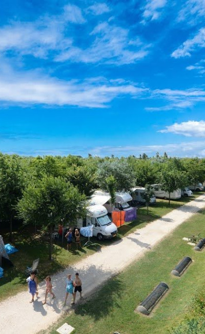 Campeggio con roulotte, piscina e persone che passeggiano sotto un cielo sereno.