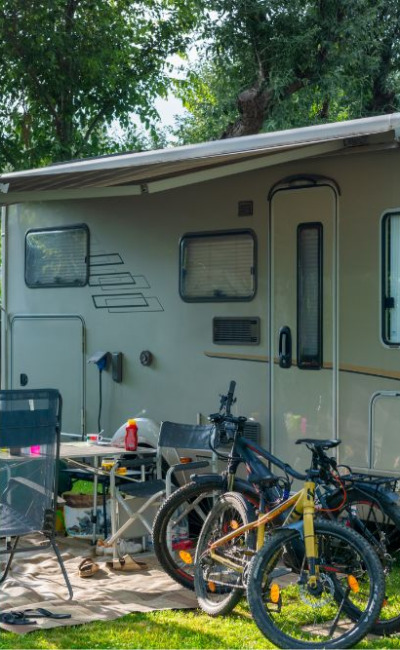 Camper con veranda, biciclette e sedie da giardino in un'area verde.