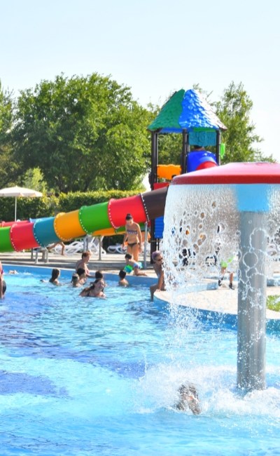 Piscina affollata con scivolo colorato e giochi d'acqua.