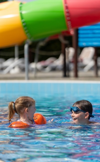 Due bambini giocano in piscina vicino a uno scivolo colorato.