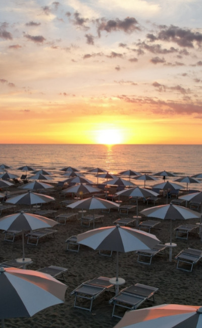 Gruppo di persone gioca a pallavolo in spiaggia sotto un cielo sereno.