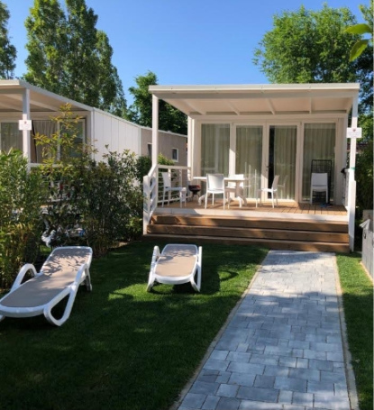 Bungalow moderno con veranda, sedie a sdraio, giardino curato e sentiero in pietra.