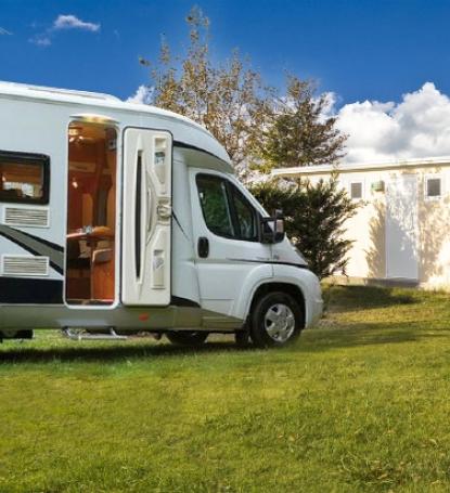 Camper parcheggiato su prato vicino a un edificio, cielo sereno e soleggiato.