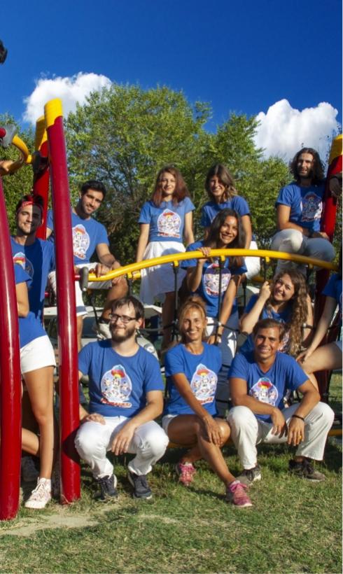 Gruppo di persone sorridenti in magliette blu, seduti su una struttura da gioco all'aperto.