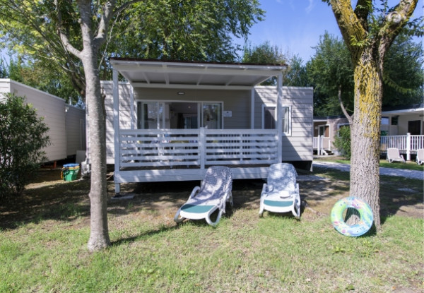 Casa mobile con veranda, due sdraio e ciambella, immersa nel verde.