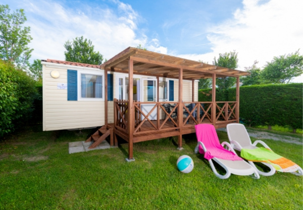 Casa mobile con veranda in legno, due sdraio e pallone su prato verde.