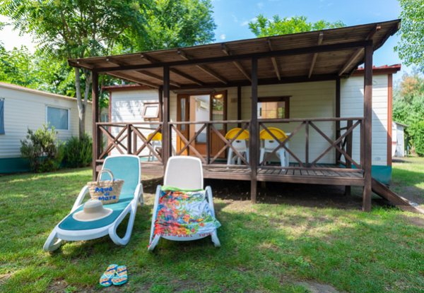 Veranda moderna con tavolo e sedie su prato verde, circondata da alberi.