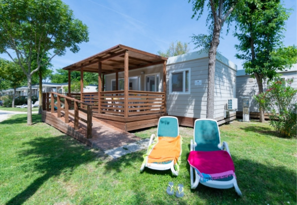 Bungalow con veranda in legno, sdraio e asciugamani colorati su prato verde.