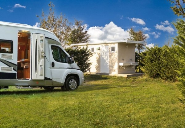 Camper parcheggiato su prato vicino a un edificio, cielo sereno e soleggiato.