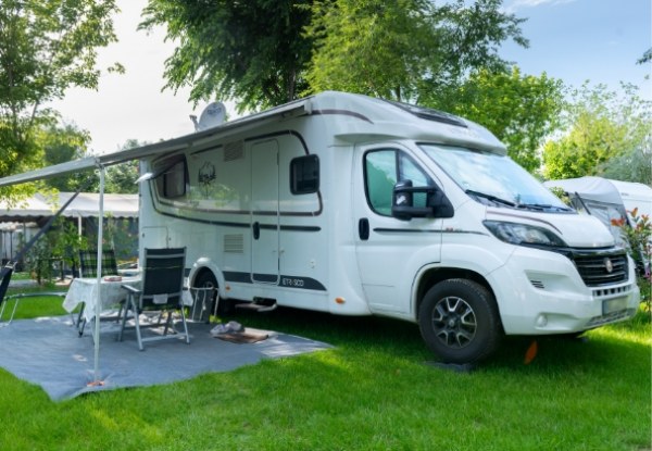 Camper bianco parcheggiato su prato verde con tavolo e sedie all'aperto.