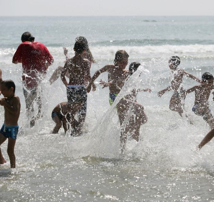 Bambini giocano e spruzzano acqua al mare in una giornata soleggiata.