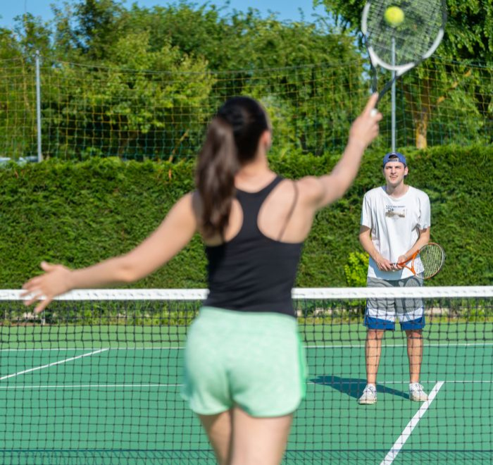 Due persone giocano a tennis su un campo all'aperto in una giornata soleggiata.