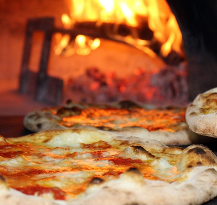 Pizze cotte in forno a legna con fiamma viva.