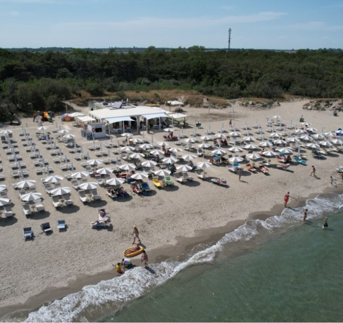 Spiaggia attrezzata con ombrelloni e lettini, vicino a un chiosco, mare calmo.