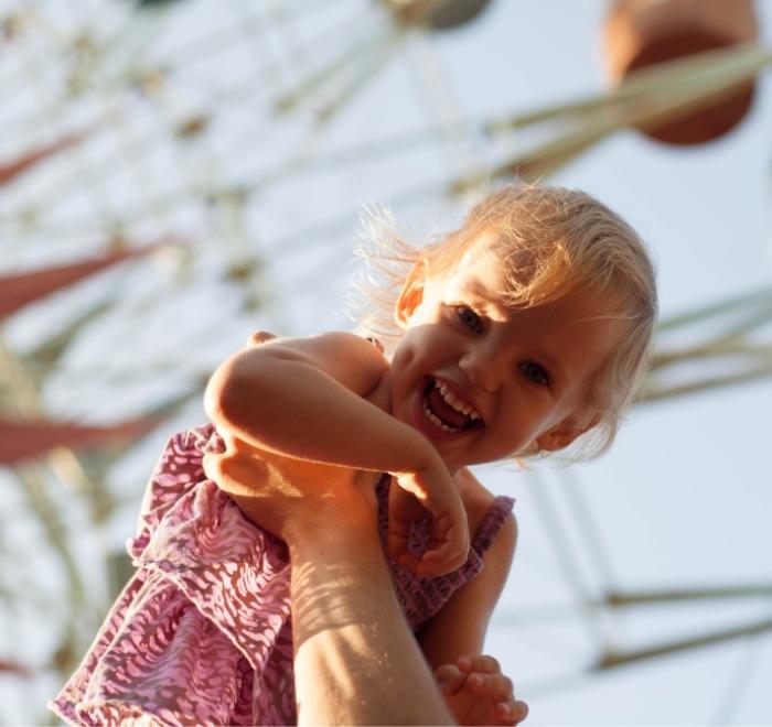 Bambina sorridente sollevata in aria davanti a una ruota panoramica.