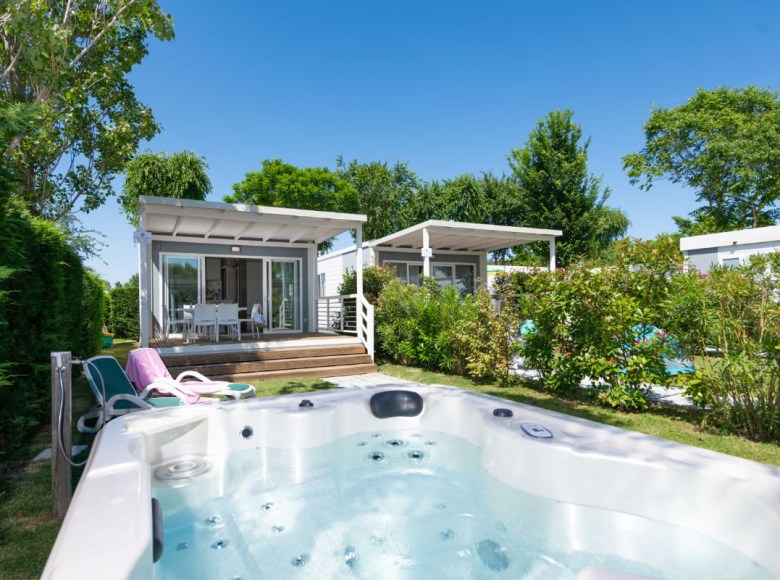 Bungalow moderno con vasca idromassaggio, circondato da verde e cielo azzurro.