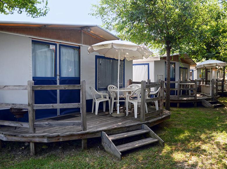 Bungalow met terras en parasol op een met bomen omzoomde camping.