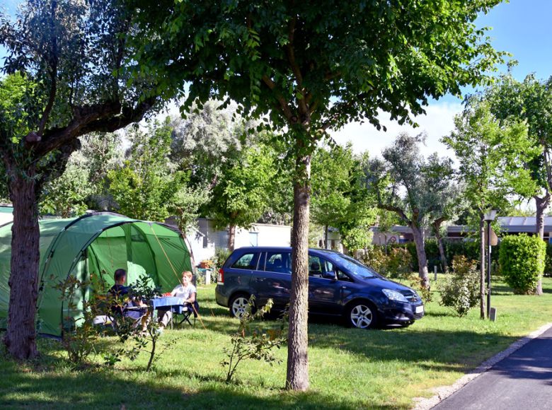 Campeggio con tenda verde, auto e persone che mangiano all'aperto.