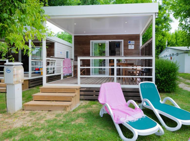 Moderne bungalow met veranda, ligstoelen en groene tuin.