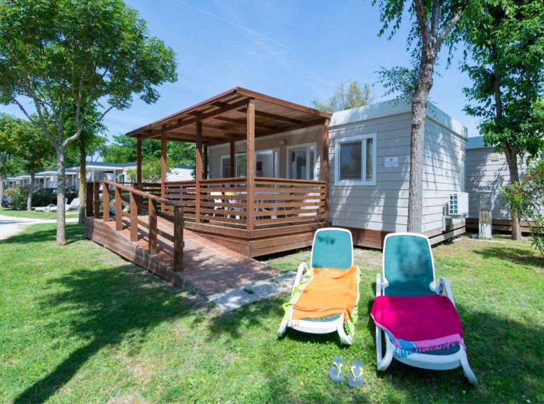 Bungalow met veranda en ligstoelen in een zonnige, groene omgeving.