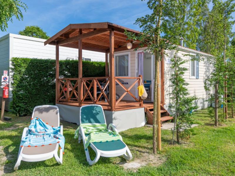 Stacaravan met houten veranda, ligstoelen en groen grasveld.