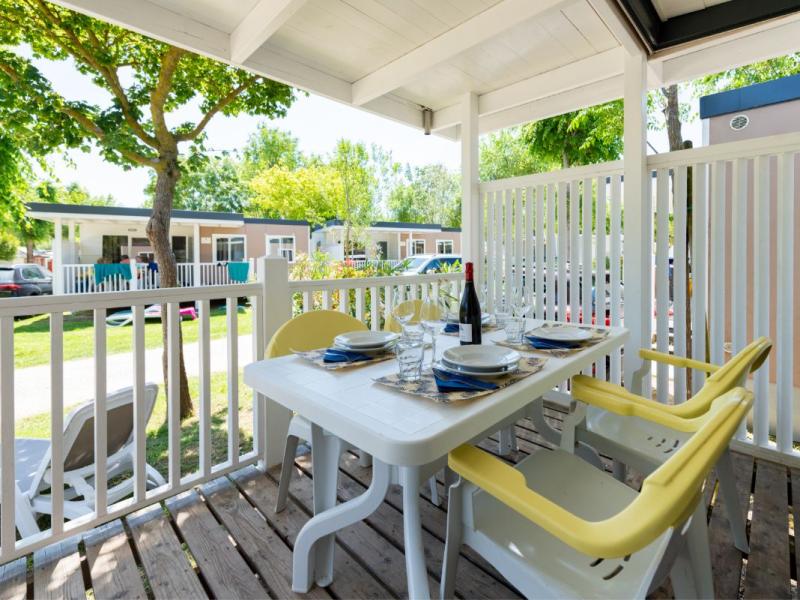 Veranda met gedekte tafel, gele stoelen, uitzicht op stacaravans.